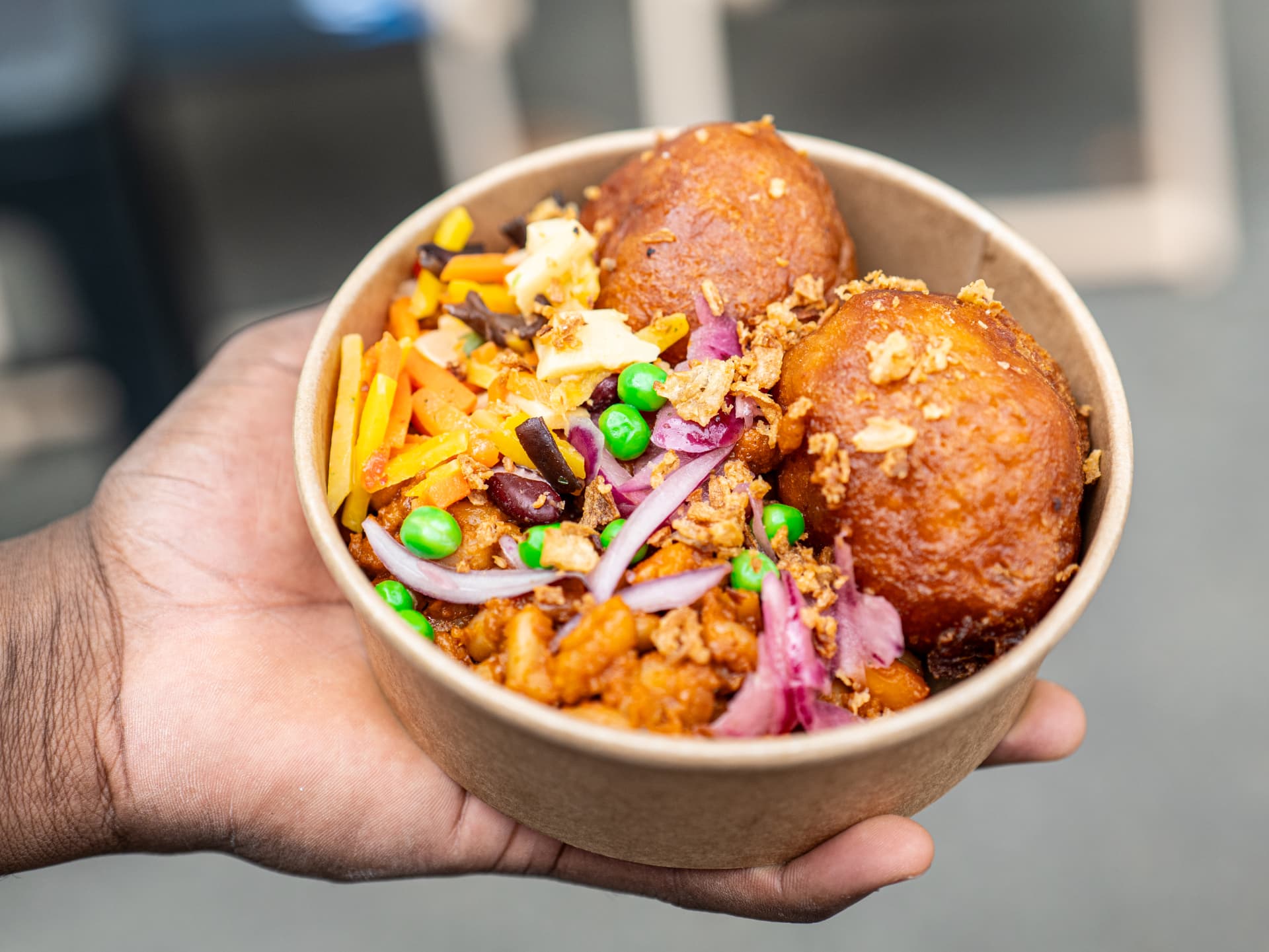 Un bol garni de beignets dorés et de légumes, tenu à la main